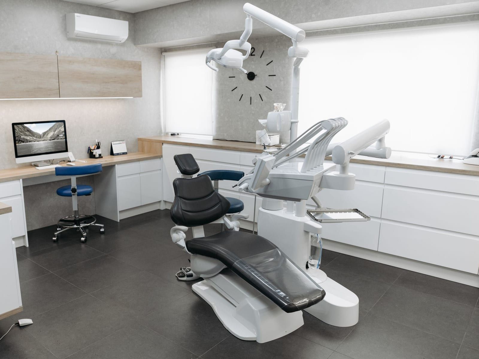 A bright treatment room with a dental chair, a desk and a large wall clock